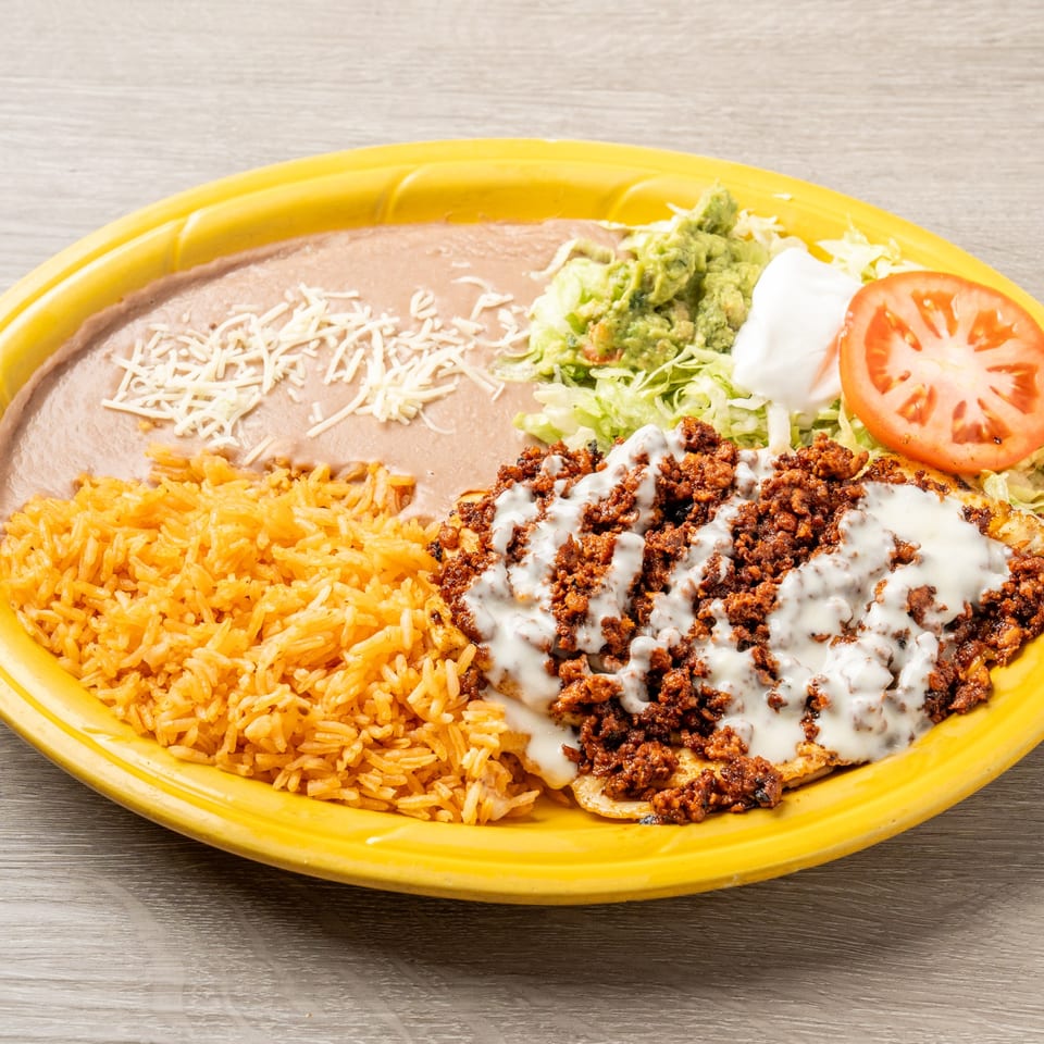 Mis Arcos Mexican dish with rice, refried beans, ground meat, guacamole, and a tomato slice.