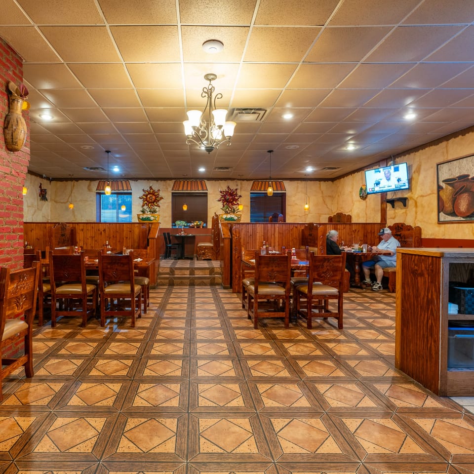 The interior of Mis Arcos Mexican Restaurant features tiled floors, wooden tables, and booths with patrons dining.