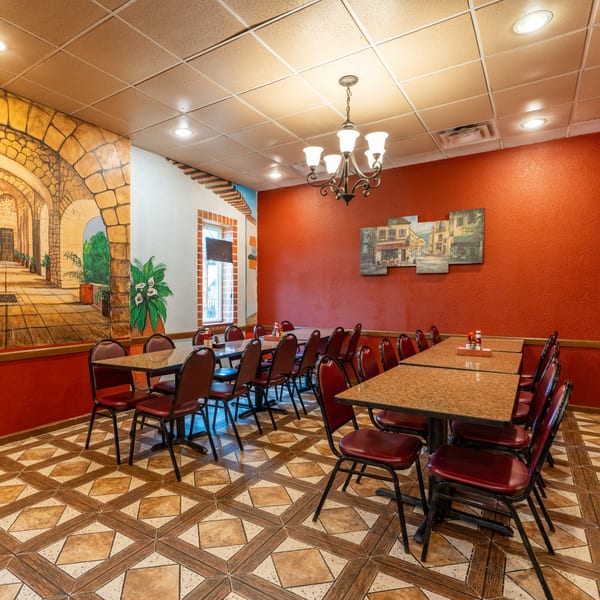 Mis Arcos Mexican Restaurant dining room with red walls, murals, and tables with red chairs.